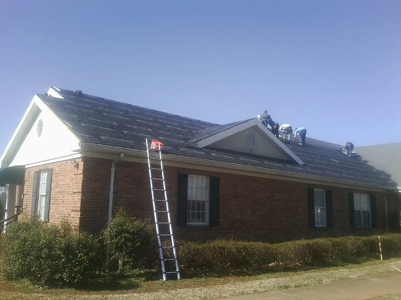 Crew tearing shingles off a brick ranch roof with a ladder set — Emergency Roof Repair work by our crew in Southampton