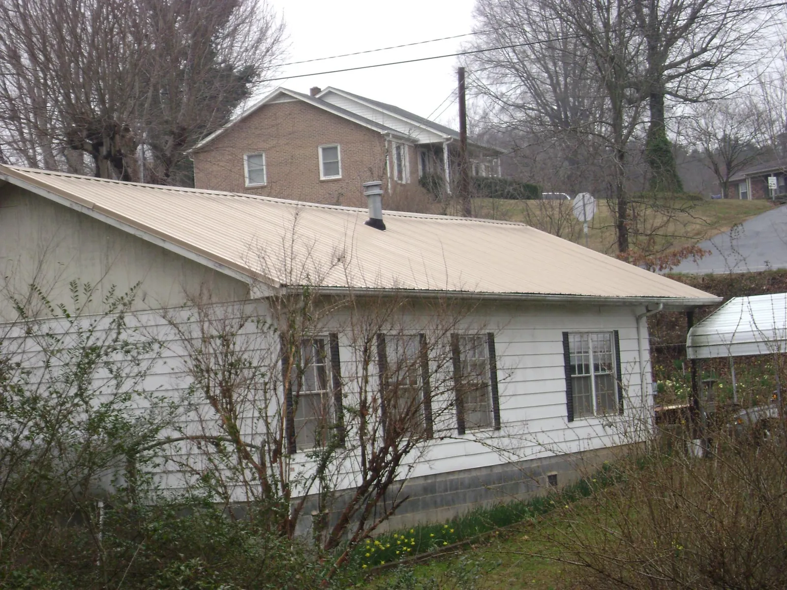 Tan metal roof on a white sided house set into a hillside — Commercial Roofing by Roofing Brothers in Southampton